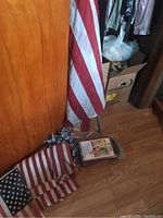 American flags displayed near closet door, one mounted on a wooden pole, folded second flag laying on floor with several patriotic pinwheels nearby