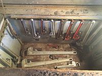 Collection of various sized pipe wrenches arranged on the floor showing heavy rust and wear