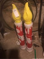 Front view of two tall electric Christmas candles with yellow flame tops and red bodies featuring white wax drip and poinsettia details.