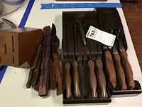 Wooden knife block, loose knives, and two black Cutco storage racks with knives.