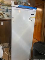 Full view of upright freezer showing white exterior and blue tape on top edge, providing an overall view of the freezer's condition and size.