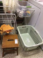 Photo showing laundry baskets, white metal wire rack, wooden stool, and part of a wooden table near a laundry area