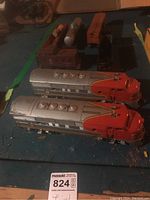 Two Lionel Santa Fe locomotive engines in silver and orange on a blue surface with additional train cars behind them.