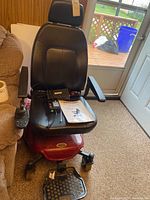 Front view of the Shoprider Streamer Sport 888WA medical power wheelchair, showing black seat, armrests, joystick controller, charger and owners manual placed on seat.