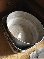 Stack of three square galvanized metal tubs with handles on short sides, showing signs of use and rust. Positioned on carpeted floor.