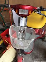 Front view of red riding scooter with white metal basket and license plate area, yellow seat partially visible