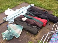 Multiple rolled items including camping tent in black rolling case and various camping chairs in bags of different colors lying on the grass and paving stones.