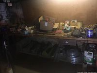 Workbench with scattered tools, tool boxes, fishing gear, and accessories under poor lighting