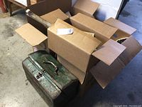 Wide view showing vintage green metal toolbox with open cardboard boxes containing tools and accessories