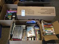 Box full of multiple VHS tapes and DVDs with varied titles visible including 'Miracle in the Hills'.