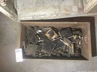 Top view of a wooden box filled with assorted vintage door hardware including hinges, locksets, and doorknobs scattered inside. Items appear worn and dusty.