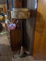 Full view of vintage floor lamp standing next to wooden cabinet against paneled wall.