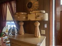 Pair of two vintage matching table lamps on a beige dresser against wooden panel wall, 24 inches tall, with starburst sunburst clock behind.