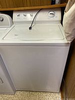 Front view of a white top loading washing machine with a closed lid and power cord resting on top.