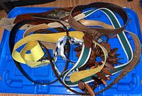 Eight different belts in a pile on a blue container lid showing assortment of styles and materials