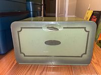 Front view of the green metal breadbox showing scratches and decorative trim