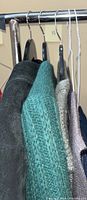 Clothing items hanging on rack including dark suede jacket, green cardigan, knit sweater vests.