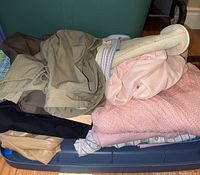 Pile of assorted women's clothing including sweaters, shirts, a belt, shorts, and skirt in various pastel and neutral colors.