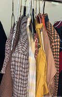 Side view of hanging mixed clothing items including shirts, blouses, vests, and blazers in various patterns and earth tones.