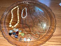 Top view of costume jewelry laid out on an amber glass tray including multiple necklaces, bracelet, rings, and pendants in various colors and styles.