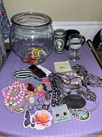 Clear glass fishbowl holding assorted buttons, surrounding costume jewelry and accessories on table
