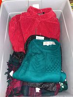 View from top of bin containing layered festive clothing items showing red corduroy fabric and teal knitted sweater
