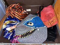 Photo of Halloween costume pieces showing dinosaur mask, red devil mask, orange and black striped fabric, colorful shiny bows, and other costume accessories.
