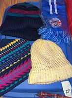 Blue tray displaying a yellow knit hat, a striped black/red/green/blue knit hat, a blue scarf with white stripes and Toronto Blue Jays logo, and a red item partly visible