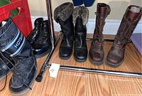 Four pairs of ladies boots including Sorel winter boots with fur lining, black combat boots, dark brown lace-up boots, and black/gray Hotsand winter boots arranged on wooden floor near metal rack.
