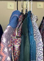 Five vintage women's clothing items hanging on a rod including a blue and pink knit sweater, floral blouses, and dresses.