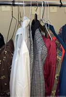 Hanging clothing pieces including white shirts, gray plaid jacket, red trousers, patterned skirts, and brown jacket.