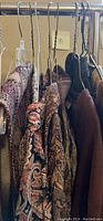 Photo of hanging clothing items on a rack showing vests, blouses, and sweaters in various patterns and solid colors.
