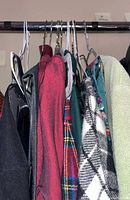 Side view of assorted women’s clothing items on hangers showing colors, patterns, and textures including handmade plaid vest and fuzzy sweater.