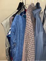 Photo showing various men's outerwear hung on a rack including a tan vest, patterned sweater, plaid and solid shirts, and jackets.