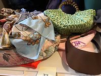 Photo of green woven handbag with bead handles, pink leather floral tote, Triangl visor, and scarves.