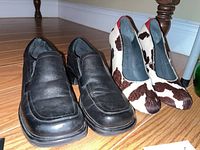 Pair of black slip-on loafers on a wood floor under furniture legs
