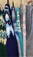 Side view of the sweaters and vest hanging on hangers, highlighting color and knit pattern variety.