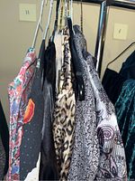 Clothing items on hangers, showing variety of patterns including floral, leopard, black satin, and paisley designs.