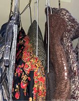 Photo showing various sweaters and patterned clothing items hanging, including brown knitted sweater and colorful patterned skirts.