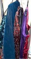 Hangers holding a collection of velvet dresses and tops in various colors including dark blue, black, red, and purple.