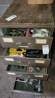 Overview photo showing open metal drawer unit with various tools and items inside including drill, sander, and assorted tools.