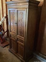 Full view of the wooden storage cabinet showing upper and lower doors with floral carvings and crown molding on top