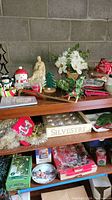 Full view of shelf with various Christmas decorations including floral arrangement, cookie jar, serving dishes, tins, and other holiday items.