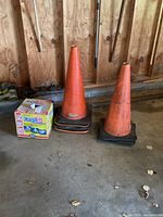 Four orange traffic cones with black bases and a partial box of Scott paper rags on the garage floor.