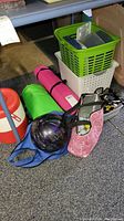 Photo showing plastic baskets, yoga mats, bowling ball, golf balls, and sunglasses items grouped on the floor beneath a table.