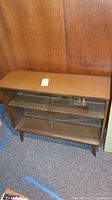Front view of vintage wooden display case showing sliding glass doors and wood veneer top with some wear.