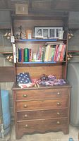 Full view of four drawer dresser with hutch containing shelves and decorated brackets, set in basement with various items present but not included in sale.