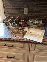 Fifteen decorative floral porcelain eggs on stands arranged on countertop beside white collector's plate and certificate spread out on the counter.