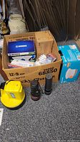 Box filled with various lightbulbs in packaging and multiple flashlights including two handheld and one large yellow Dorcy model.