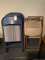 Six folding chairs arranged in two stacks: four blue metal frame chairs with striped padded seats on the left, two brown metal frame chairs with beige padded seats on the right.